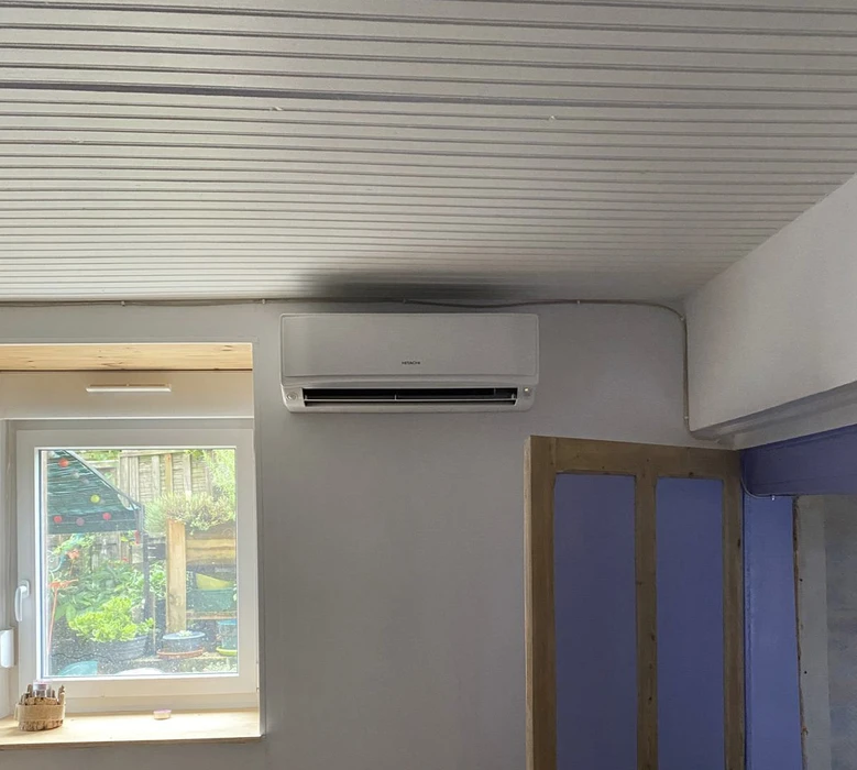Intérieur moderne avec climatiseur mural Hitachi installé au plafond, murs peints en gris clair, lambris bois au plafond