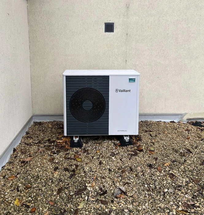 Extérieur d'un bâtiment avec installation de pompe à chaleur air-eau Vaillant positionnée sur sol gravillonné contre mur crépi beige