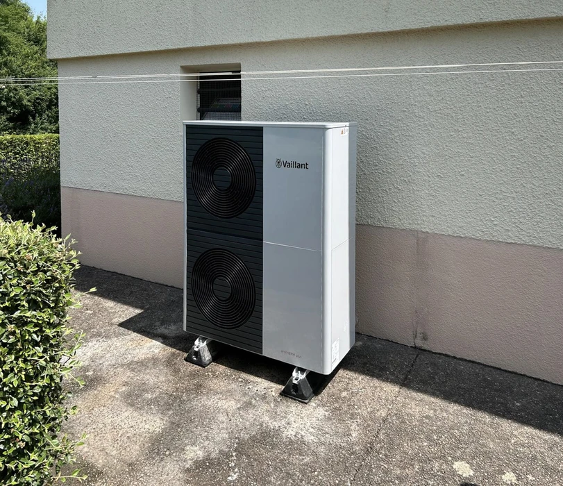 Extérieur résidentiel avec pompe à chaleur air-eau installée contre mur de maison