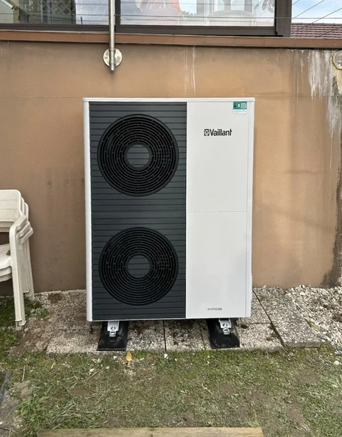 Installation extérieure d'une pompe à chaleur air-eau Vaillant dans une cour résidentielle, positionnée contre un mur beige sur dalle béton avec supports antivibratoires